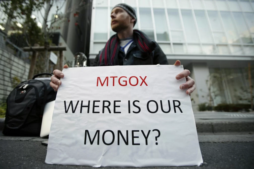 Um homem segurando uma placa escrita "MTGOX WHERE IS OUR MONEY?"